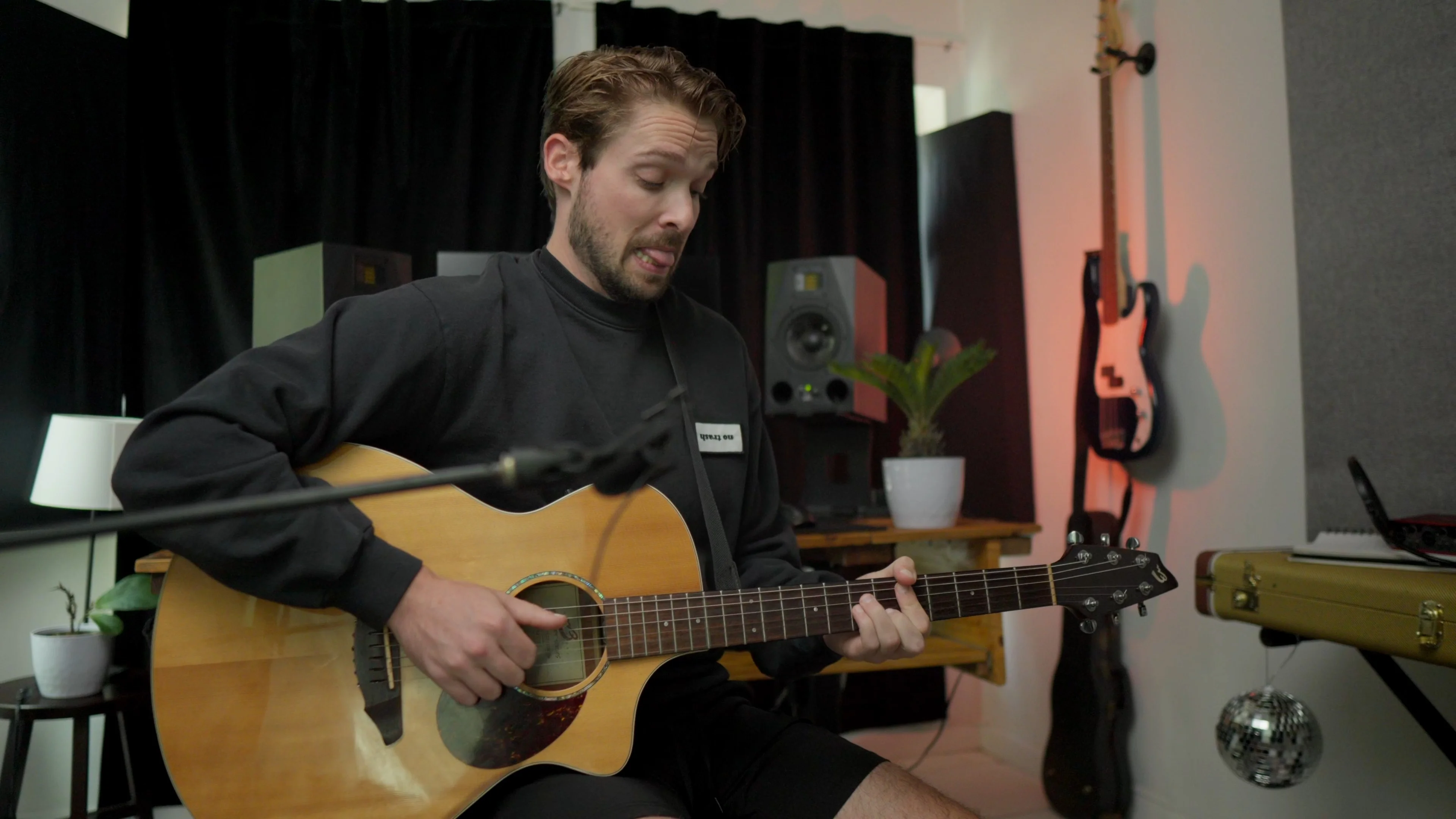 Mattie playing acoustic guitar in professional studio, focusing on a specific instrument to narrow production scope