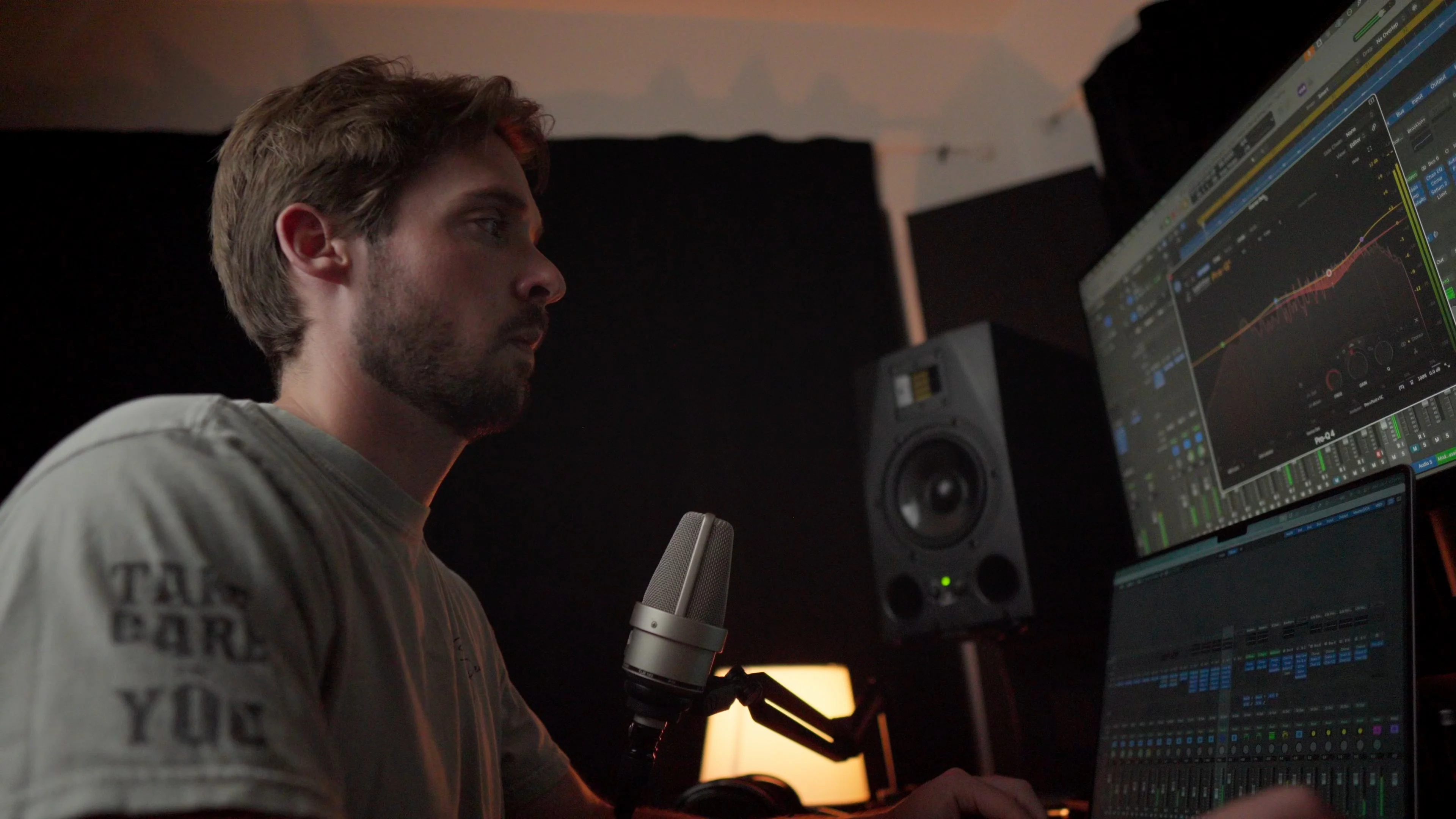 Mattie recording vocals with a condenser microphone while viewing Logic Pro on dual monitors during the DAW comparison