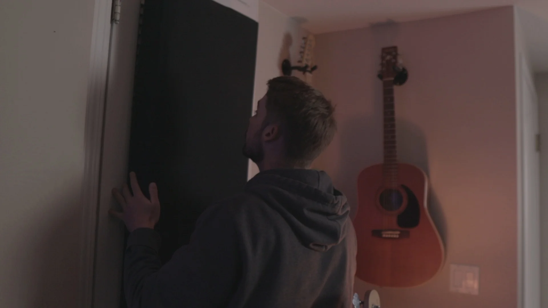 Mattie hanging DIY black acoustic treatment panels on studio wall